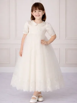 Bambina che indossa un abito da cerimonia lungo in tulle bianco con ricami in pizzo e colletto rotondo.