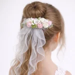 Acconciatura bambina con chignon decorato da fermaglio di fiori rosa e bianchi e velo in tulle a cascata.