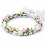 Coroncina di fiori per bambina con roselline bianche e rosa, foglioline verdi e fiocco in organza bianca per acconciatura da cerimonia.