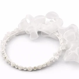 Coroncina gioiello per bambina con piccoli fiori bianchi, cristalli luminosi e ampio fiocco in organza bianca a cascata per cerimonia.