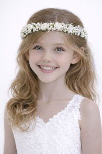 Coroncina gioiello per bambina con fitto intreccio di perle, cristalli e roselline color avorio indossata su capelli biondi mossi per una cerimonia.