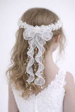 Dettaglio posteriore di lusso della coroncina W 434 con maxi fiocco in organza bianca e cascata di perle lucide pendenti su capelli mossi da cerimonia