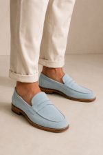 Mocassini uomo celeste in camoscio indossati con pantaloni beige eleganti su sfondo minimal neutro