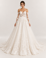 Abito da sposa principesco avorio con maniche lunghe in pizzo floreale, spalle scoperte, corsetto trasparente e ampia gonna ricamata.