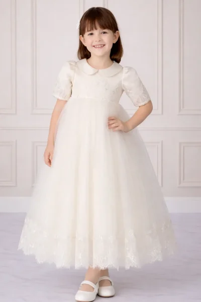 Bambina che indossa un abito da cerimonia lungo in tulle bianco con ricami in pizzo e colletto rotondo.