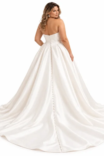 Vista posteriore di abito da sposa curvy principessa in raso avorio, con schiena scoperta, fila di bottoncini rivestiti, ampia gonna strutturata e lungo strascico elegante.